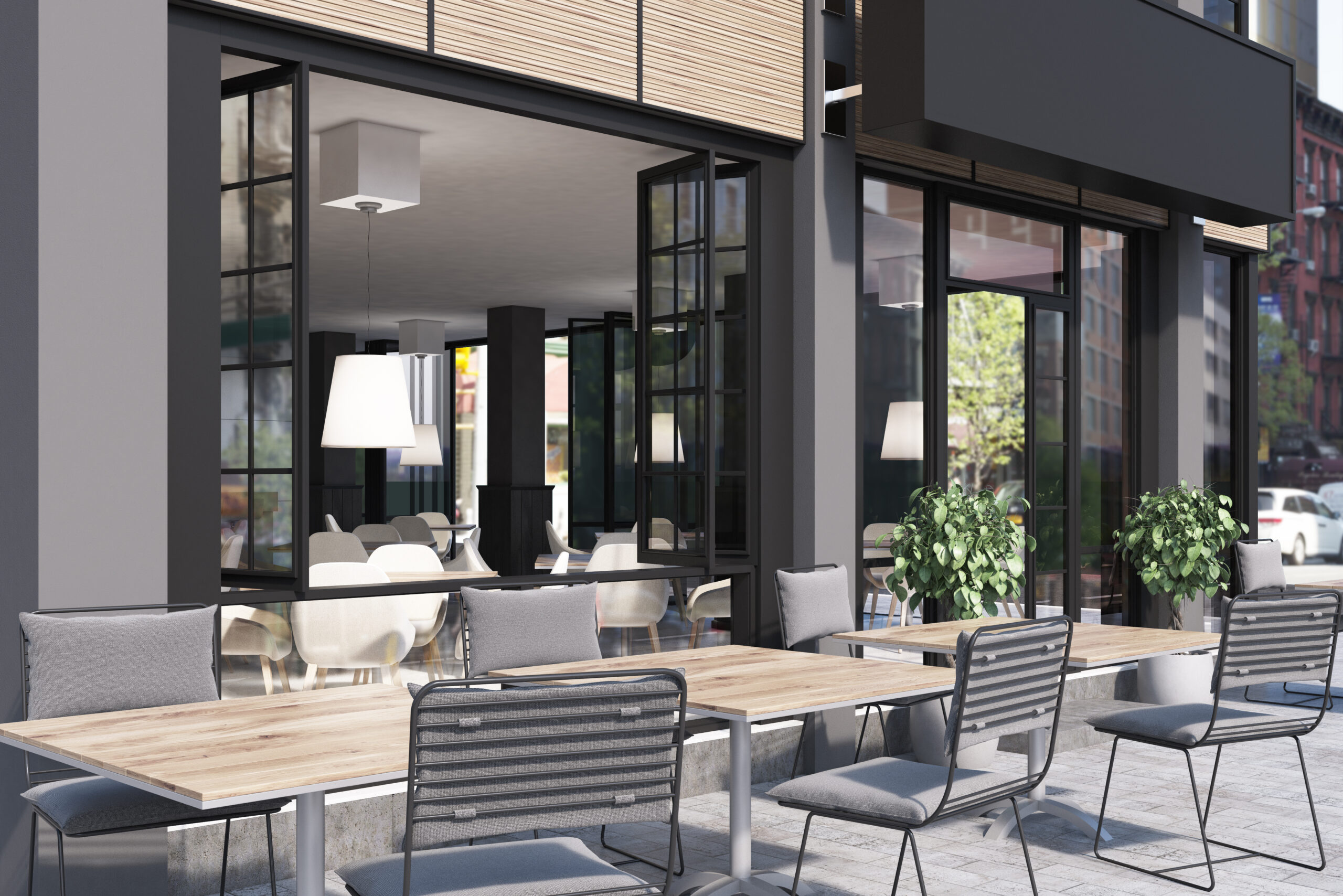 An outdoor seating area with wooden tables and cushioned chairs outside a modern business building, featuring large windows and indoor seating visible through the open glass doors.